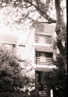 Mid-century modern multi-level building with cantilevered balconies, framed by lush greenery and mature trees. Architectural ...