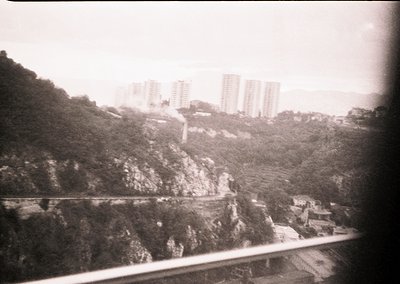Vintage black-and-white urban landscape featuring high-rise apartment blocks on a hillside, likely from the mid-20th century....