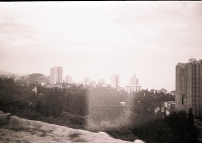 Urban skyline with mid-rise buildings and dense greenery, likely from a 1960s–1970s monochrome photograph. Fog or mist obscur...