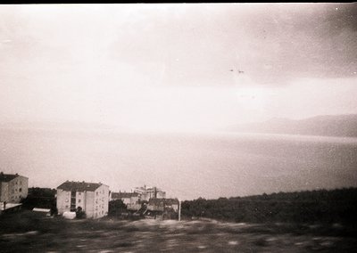 Mid-20th century seaside town with Soviet-era concrete buildings by the shore. Low-rise apartment blocks and a central struct...