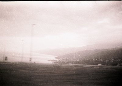 Vintage black-and-white shot of a rural landscape with power lines stretching into the distance, framing a hazy horizon. Low-...