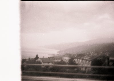 Vintage black-and-white train window view of rural landscape, featuring misty hills and scattered buildings. Likely mid-20th ...