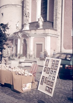 Baroque-style church façade with sculpted religious figures and arched doorway. Outdoor market stall displays vintage postcar...