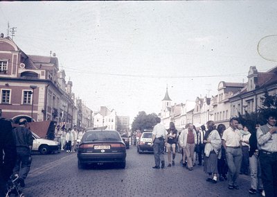 Vintage street scene with cobblestone road, mid-20th century European architecture, and dense pedestrian traffic. A mix of vi...