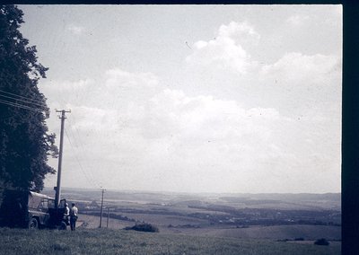 Vintage black-and-white rural landscape featuring a lone utility pole and two figures near a vintage truck on a grassy hillsi...