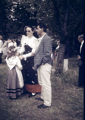 Mid-20th century outdoor gathering with formal attire: man in checkered blazer, white trousers, and sunglasses shaking hands ...