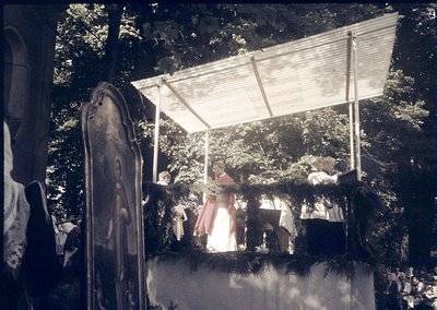 Vintage outdoor stage with wooden canopy and draped fabric, featuring a woman in a 1960s-style dress performing on a raised p...