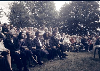 A vintage outdoor gathering of elderly individuals seated in a grassy area under trees, likely mid-20th century. Attire sugge...