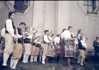 Traditional folk ensemble performing outdoors, likely Eastern European, mid-20th century. Men in embroidered vests and white ...