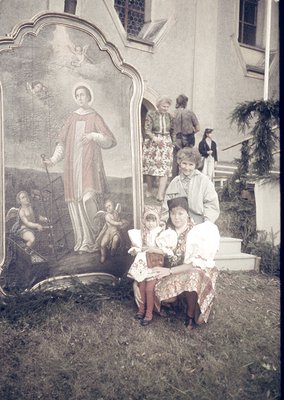 Vintage sepia-toned portrait of a woman and child seated on steps beside a religious mural depicting a saint flanked by cheru...