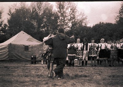 Vintage black-and-white photo of a traditional folk dance performance in an outdoor setting, likely Eastern Europe. Central m...