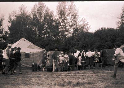 Group of children and adults in outdoor camping scene, likely 1950s–1970s. Tent with "13" marked on its side suggests organiz...
