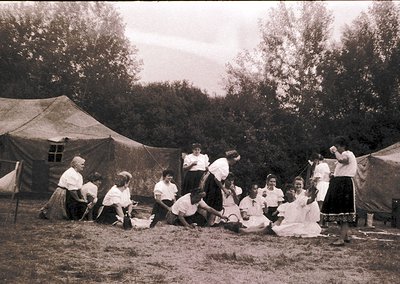 Vintage sepia-toned group photo from early 20th century, likely 1900s–1920s. Outdoor setting with tents and lush greenery, su...