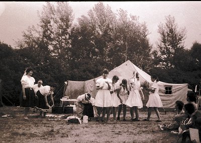 Vintage outdoor gathering in a rural setting, featuring a group of women and children in early 20th-century attire. A tent an...