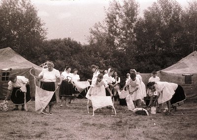 Vintage outdoor scene featuring a group of women in early 20th-century clothing, likely 1910s–1920s, performing a traditional...