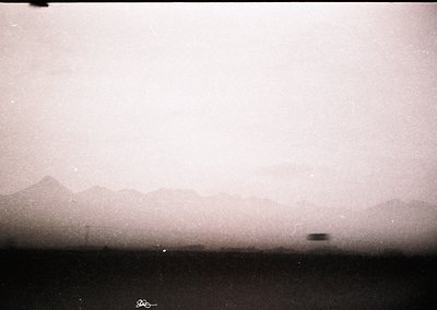 Vintage sepia-toned landscape shot through a window or film grain, revealing faint mountain silhouettes and a distant aircraf...