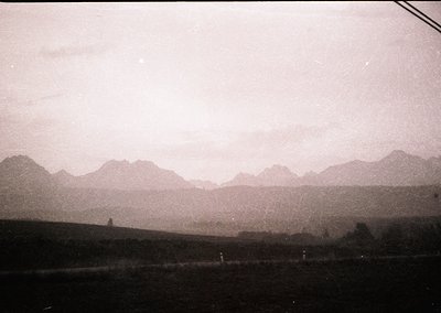 Vintage sepia-toned landscape featuring jagged mountain range under overcast skies. Foreground shows sparse vegetation and a ...