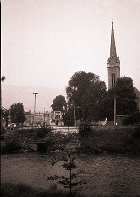 Black-and-white street scene featuring a Gothic Revival church spire with pointed arches, likely 19th-century European archit...
