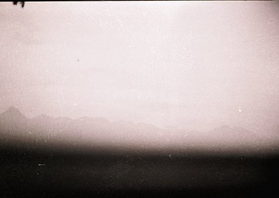 Vintage monochrome shot of a hazy coastal horizon, likely mid-20th century. Silhouetted landforms fade into mist, suggesting ...