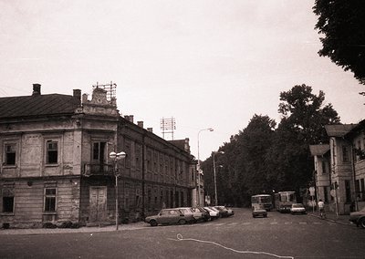 Vintage black-and-white street scene featuring Soviet-era architecture with a two-story stone building showcasing classical d...