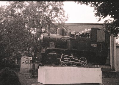 Vintage steam locomotive mounted on a concrete pedestal, likely a preserved exhibit. Visible number "157" and "1908" on the e...