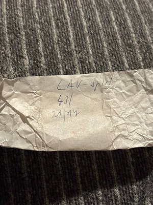 Handwritten label on crumpled paper: "LAV-Split 431 21/07" against dark fabric. Likely a vintage luggage tag or shipping labe...