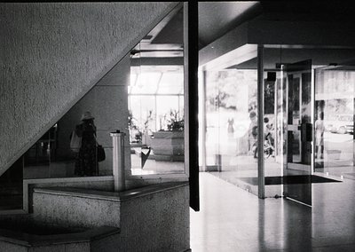 Mid-century Brutalist architecture interior: raw concrete stairwell and reception desk with geometric glass partitions. Refle...