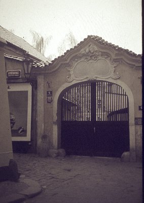 Vintage-style arched gate with ornate plasterwork and wrought-iron double doors, set in a cobblestone courtyard. Adjacent sig...