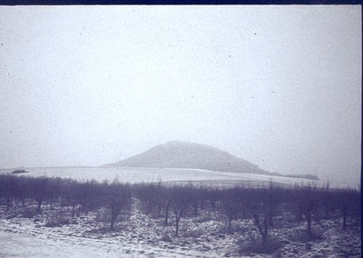 Vintage sepia-toned landscape featuring a snow-covered hillside with sparse, leafless trees in foreground. Overcast sky obscu...