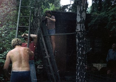 Vintage 1970s-style group water fight under a cascading waterfall in a lush forest. Three shirtless men and one partially vis...