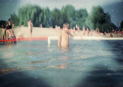 Vintage photo of a crowded beach scene with blurred motion, likely mid-20th century. Children and adults wade in shallow wate...