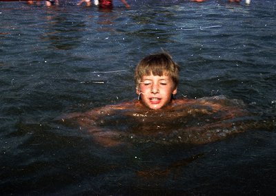 Vintage black-and-white photo of a young boy mid-dive in murky water, arms extended forward. The grainy texture and lighting ...