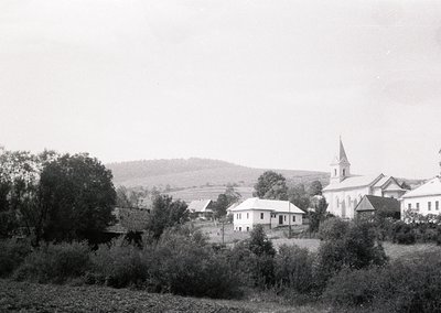 Black-and-white rural village scene featuring a prominent church with a tall steeple and whitewashed walls, surrounded by mod...