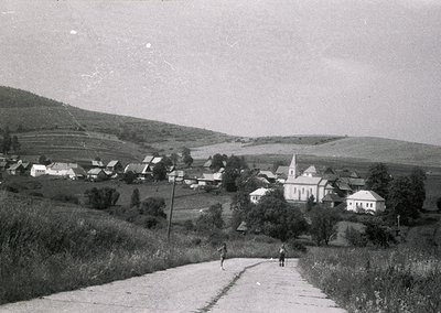 Vintage black-and-white rural village scene with a prominent church steeple and clustered houses on rolling hills. Two figure...