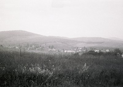 Mid-20th century rural landscape featuring scattered farmhouses and rolling hills. Low-contrast black-and-white composition h...