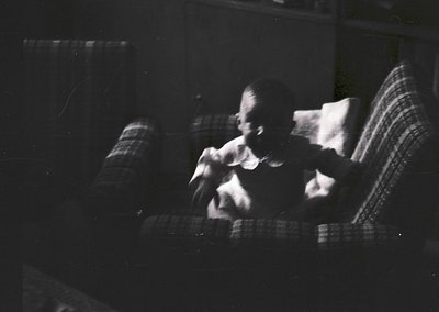 Vintage black-and-white photo of two figures seated on a striped armchair, blurred motion suggests movement or candid capture...