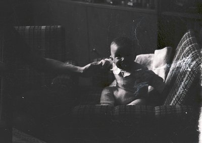 Vintage black-and-white portrait of a seated child brushing teeth in a dimly lit indoor setting, likely mid-20th century. Che...