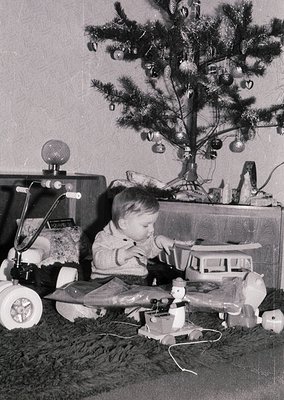Young child playing with vintage toys—steam train set and toy airplane—on a shag-carpeted floor beside a decorated Christmas ...