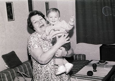 Mid-20th century indoor portrait: woman in floral-patterned dress cradles a toddler in a striped sweater, seated on a pattern...