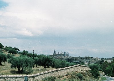 Vintage aerial view of a hillside town with a prominent Baroque-style church atop a hill, surrounded by dense olive groves. S...
