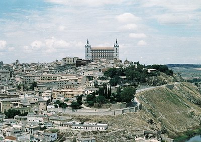 Aerial view of Toledo’s historic skyline, featuring the Alcázar perched atop a hill. Mid-20th century urban layout with clust...