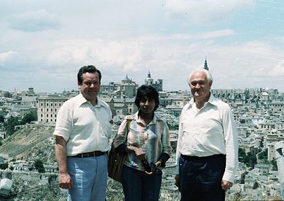 Three individuals pose on a hillside overlooking Toledo, Spain, circa 1970s. The man on the left wears a light-colored button...