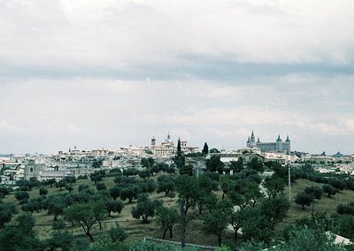 Vintage aerial view of Madrid’s skyline, featuring the Alcázar of Toledo and San Juan de los Reyes church. Lush olive groves ...