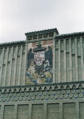 Relief sculpture featuring a crowned coat of arms with a shield displaying stacked castles and lions, flanked by seashell mot...