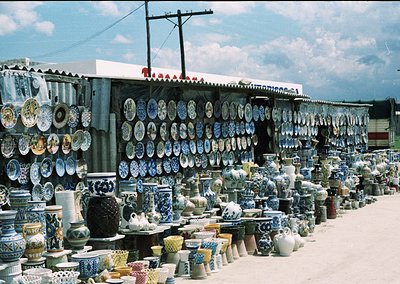 Vibrant outdoor ceramic display featuring intricately patterned plates, vases, and bowls arranged in rows along a makeshift s...