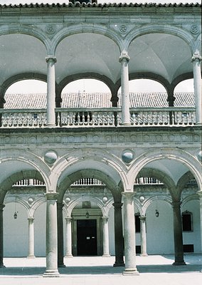 Renoir-style courtyard with double-tiered arcades featuring classical columns, balustrades, and spherical finials. Stonework ...