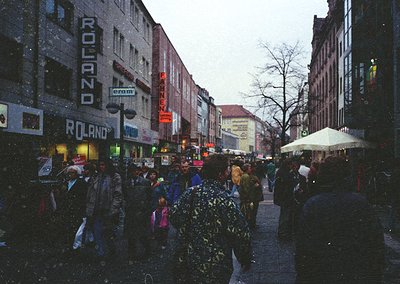 Vintage urban street scene with heavy snowfall, bustling pedestrians in winter attire. Prominent Roland and Pannen stores on ...