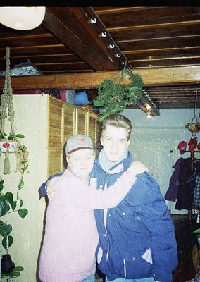 Vintage indoor portrait of two individuals in casual winter attire—man in a blue denim jacket and red cap, woman in a pink sw...