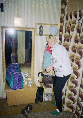 Woman in a retro-style sweater poses indoors beside a mirrored wall, holding a brown handbag. Surrounding her: a wrapped gift...