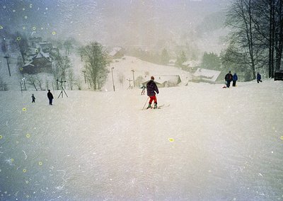 Vintage ski slope scene with heavy snowfall, featuring skiers in 1960s-70s gear. Snow-covered village and forested hills in b...